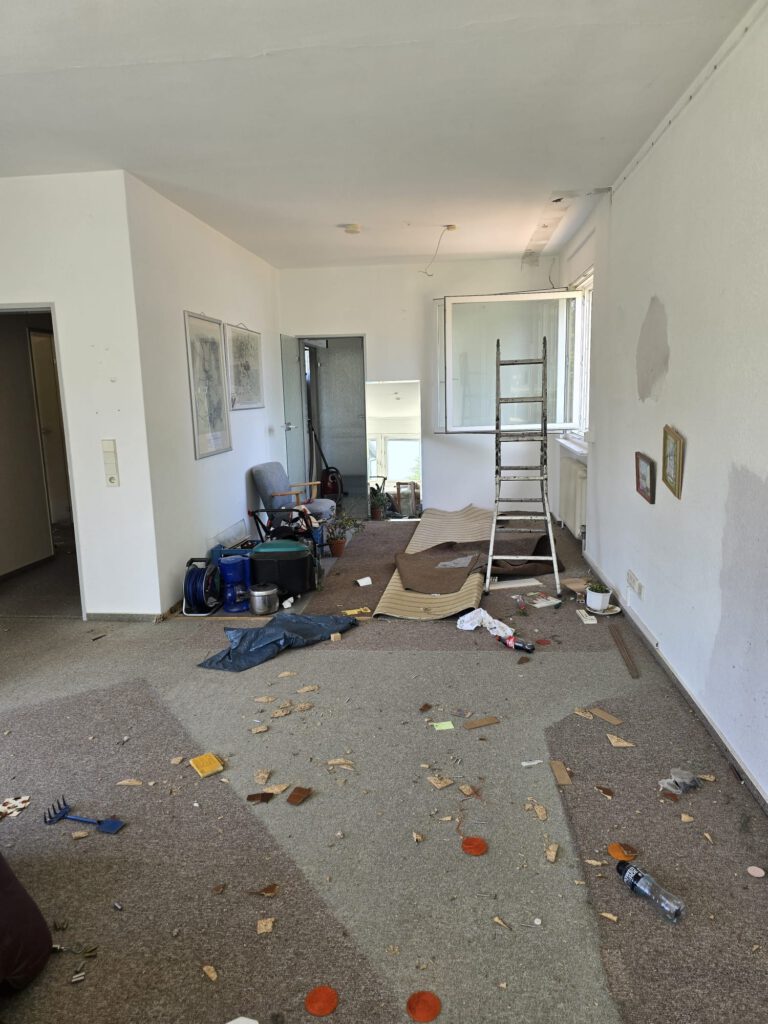 Wohnzimmer – vor der Räumung → Sperrmüll, Teppichreste und persönliche Gegenstände noch vorhanden.