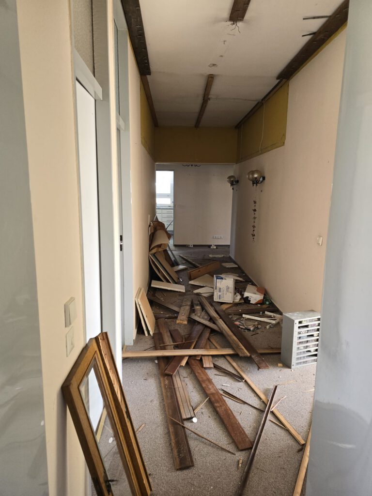 Langer Flur – vor der Entrümpelung → Vollgestellt mit Holzresten, Teppichboden stark verschmutzt.